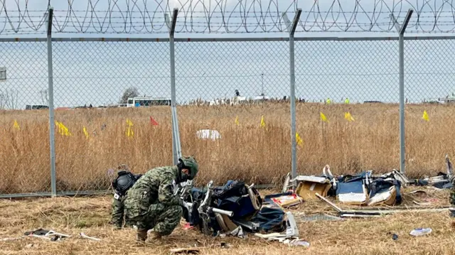 Soldier bends down to inspect large piece of debris from plane