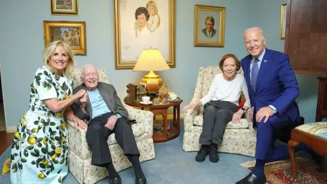 Left, Jill in a dress decorated in lemons, kneels by an armchair in which Jimmy sits. On the right, Biden in a blue suit kneels beside Rosalynn's armchair