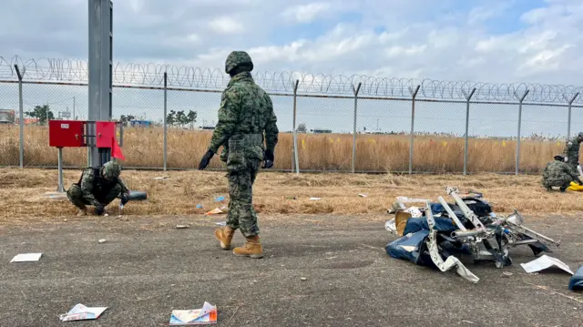 Soldier walking towards another soldier who is crouched down inspecting plane debris