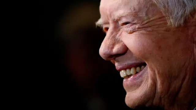 Jimmy Carter smiling on a black background