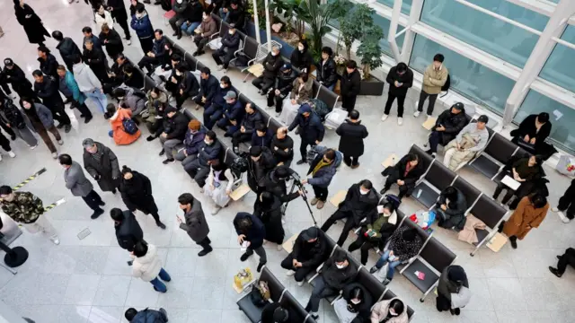 Crowd of people in an airport, some sat on seats some standing, aerial view