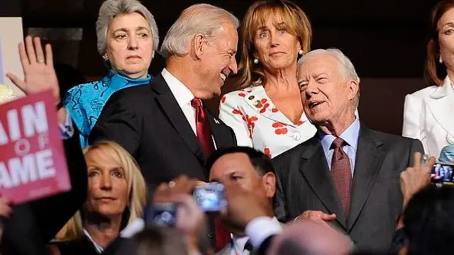 Photographed within a crowd, Biden smiles as he looks at Carter, who speaks