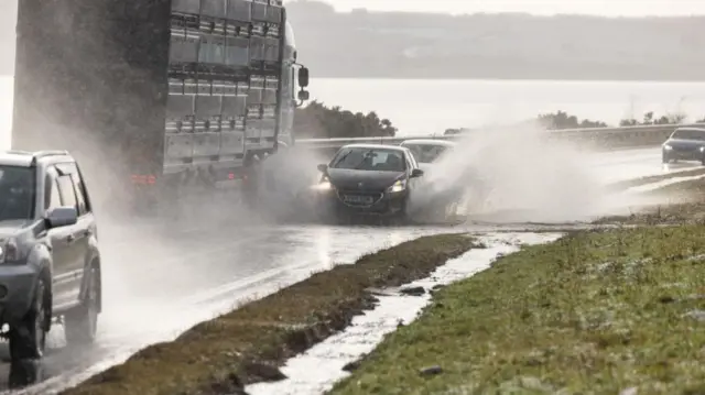 A car going through a puddle, sending huge sprays of water out each side