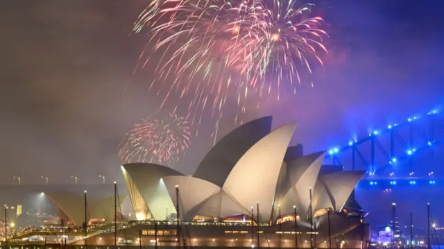 A close up of pink and green fireworks lighting up the sky around the Sydney Opera House