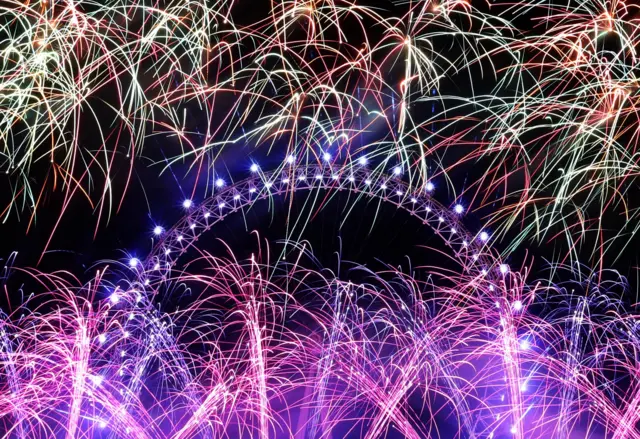 Pink and purple fireworks in the sky surrounding London Eye