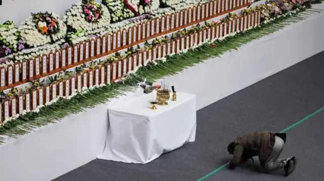 A man kneels as he pays tribute to the victims at a joint memorial altar set up at a stadium in Muan