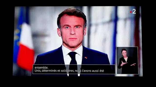 French President Emmanuel Macron seen delivering his new year address on TV