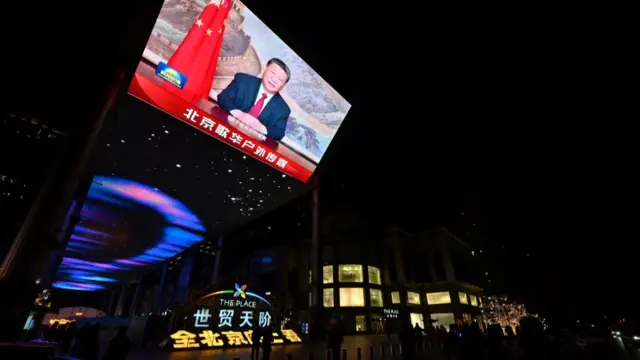 President Xi Jinping shown on a screen in his annual address to the nation. He is wearing a suit and red tie and appears in front of a Chinese flag.