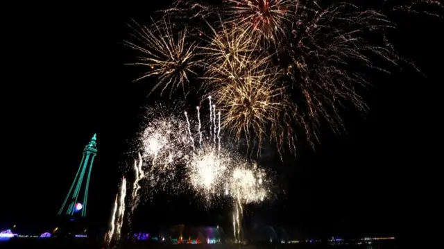 Fireworks going off in front of the Blackpool Tower in the darkness, which is illuminated with blue lights