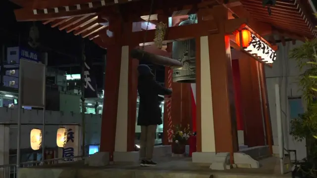 Red Temple structure  with a bell inside, with one person stood in front