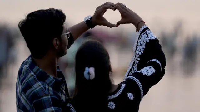 A couple forms a heart shape with their hands on Juhu beach in Mumbai