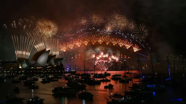 Fireworks above Sydney Harbour Bridge and Sydney Opera House, with dozens of boats in front in the darkness