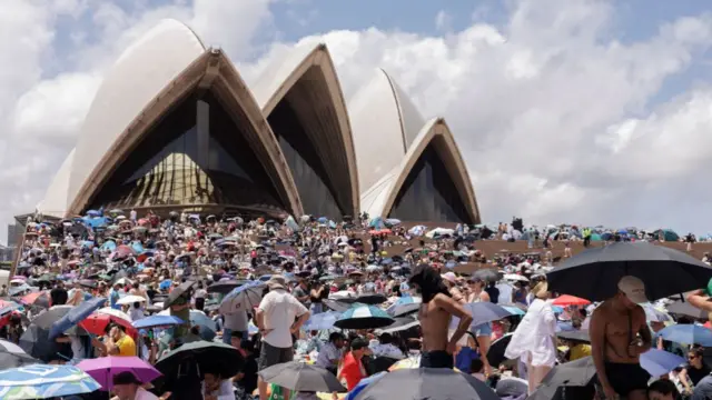 Dozens of people sat with umbrellas in front of Sydney Opera House