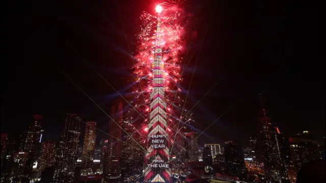 Red fireworks shoot off of the Burj Khalifa which is lit up with the words "HAPPY NEW YEAR FROM THE UAE"