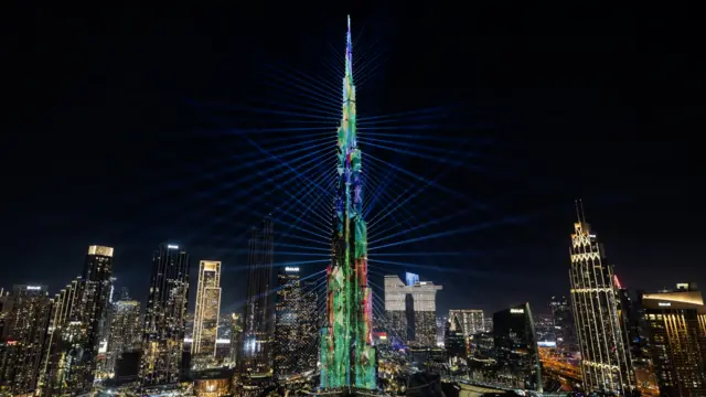 A light display beams from the Burj Khalifa at night amongst the Dubai skyline.