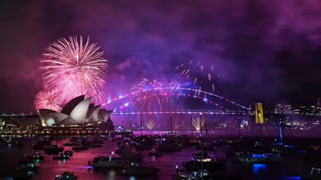 Pink and purple fireworks light up the Sydney skyline with the Opera House and Sydney Harbour Bridge in vision.