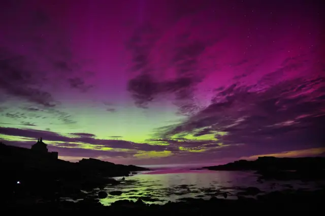 Purple and green dews fill the cloudy sky over a body of water in Northumberland