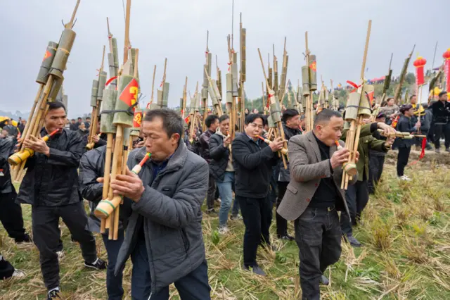 Villagers blow on reed wind instuments