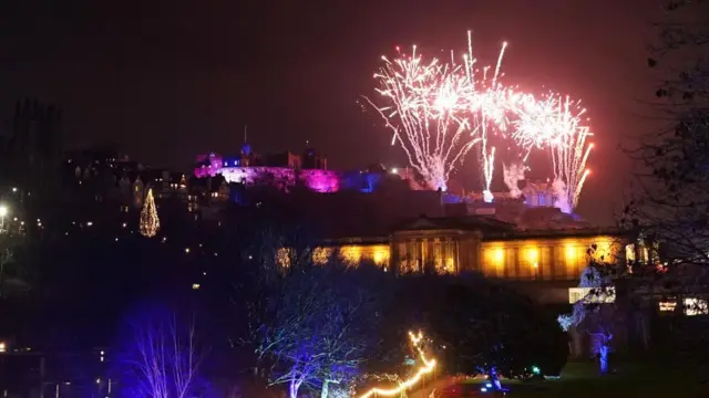 A firework display over Edinburgh Castle. The caste is highlighted in purple light