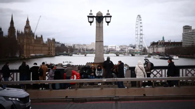 People on Lambeth bridge look across to Westminster and the London Eye