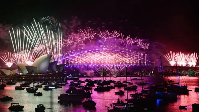 Fireworks above Sydney Harbour Bridge and Sydney Opera House, with dozens of boats in front in the darkness