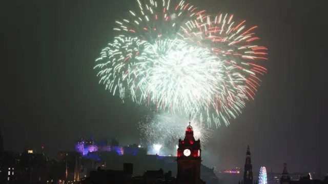 The Balmoral Hotel's clock tower takes centre stage in this picture of Edinburgh's city centre's skyline as red and green fireworks go off in the background. Edinburgh Castle, lighted in purple and blue, is visible in the bottom left of the image