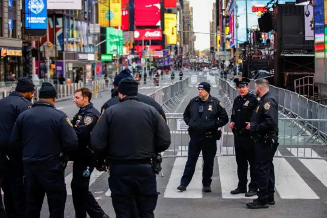 Police mill about in the middle of Times Square. There's large billboards with advertising all over the background and metal barriers