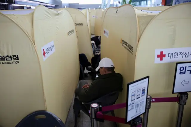 A man in a white cap is sat inbetween temporary beige tents put up at Muan International Airport