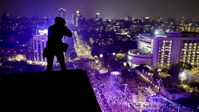 A person on top of a building, who appears as a shadow, takes photos of crowds below attending New Year's Eve celebrations in Taiwan