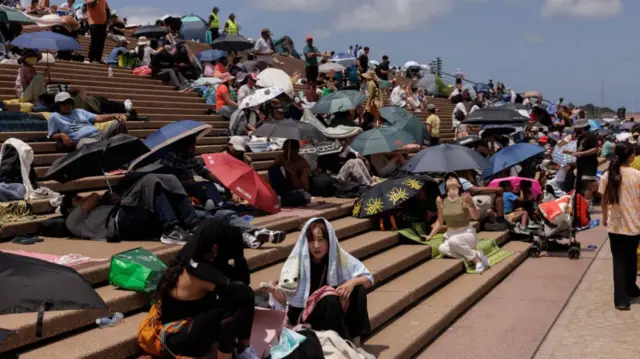 People sat on the steps in front of Sydney Opera House with umbrellas