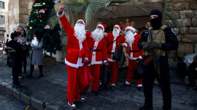 An armed man guards people dressed as Santa