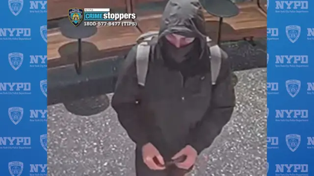 A still from security footage shows a  person is wearing a black jacket, a black balaclava covering the lower half of their face, and a grey backpack