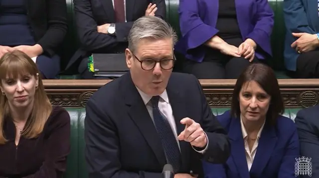 Keir Starmer facing camera in a suit with finger pointing, with Labour MPs sat behind him in House of Commons