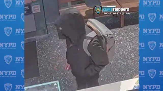 A still from security footage shows a  person is wearing a black jacket, a black balaclava covering the lower half of their face, and a grey backpack