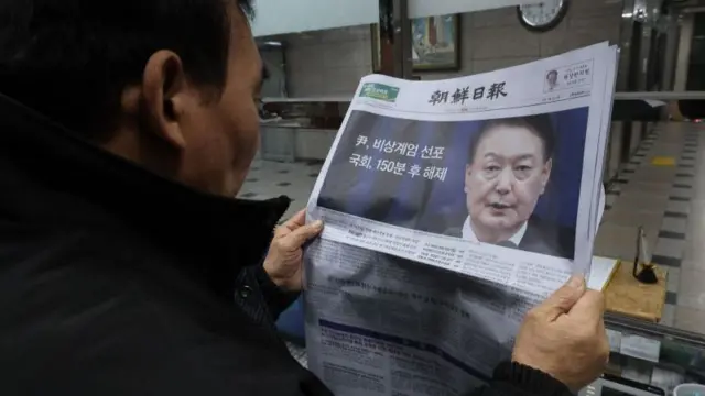 A man looks at a newspaper reporting South Korean President Yoon Suk Yeol announced his intention to lift the emergency martial law in Seoul, South Korea