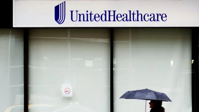 A woman walks past the UnitedHealthcare office, New York, with blue text