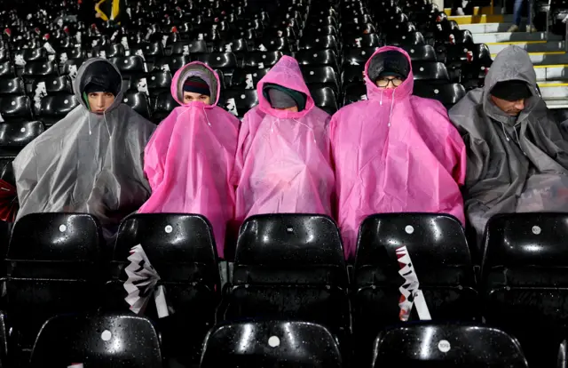 Fans sit in rain ponchos at Craven Cottage