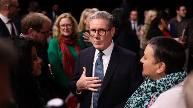 Keir Starmer chats to two women either side of him, while other people stand nearby