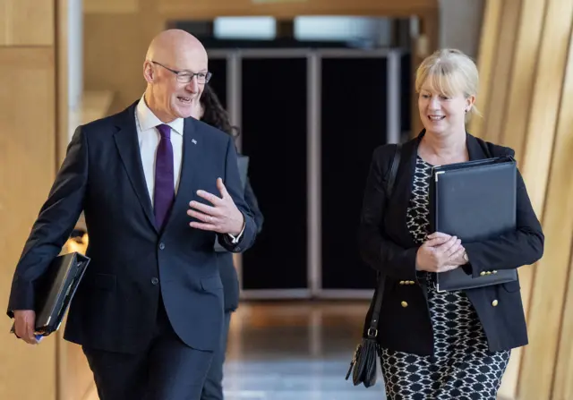 First Minister John Swinney and Finance Secretary Shona Robison walk towards Holyrood's chamber, carrying binders