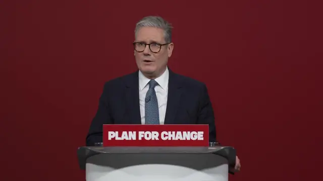 Keir Starmer delivers his 'Plan for Change' speech in a suit in front of a red backdrop, behind a podium