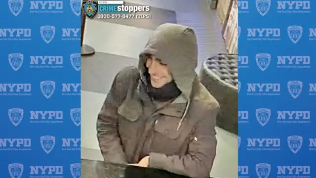 A CCTV image of a person in a store wearing a jacket with a hood up and smiling