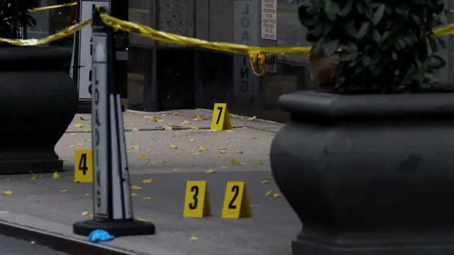 Yellow signs with numbers on them are on a pavement which is surrounded by yellow crime scene tape