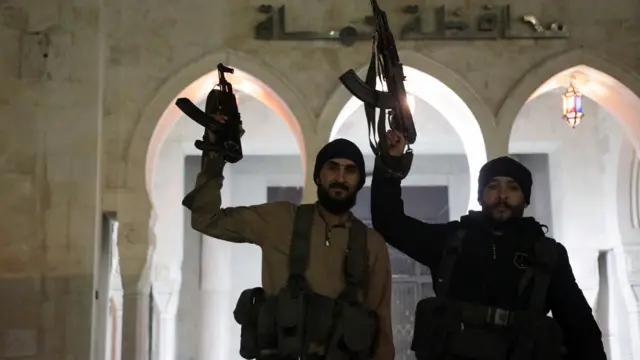 Rebel fighters hold weapons in front of Hama governor's building as they gather after Syrian rebels captured the city during their advance across northern Syria, in Hama, Syria December 5, 2024.