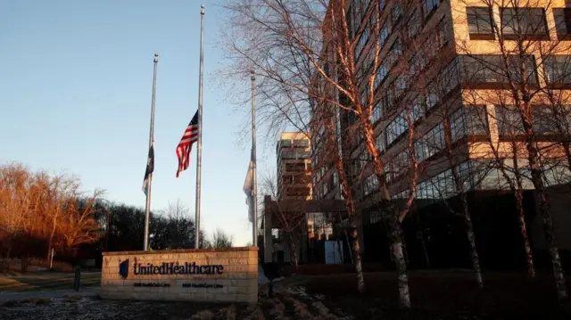 Flags at half mast above a sign indicating 'UnitedHealthcare'