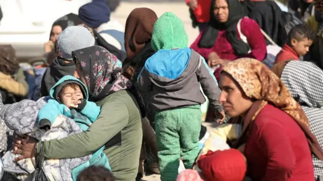 Women and children sitting outside, wearing winter clothing, in Taqba after fleeing Aleppo. Taken 4 Dec.