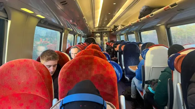 Passengers sit in red seats in a train carriage