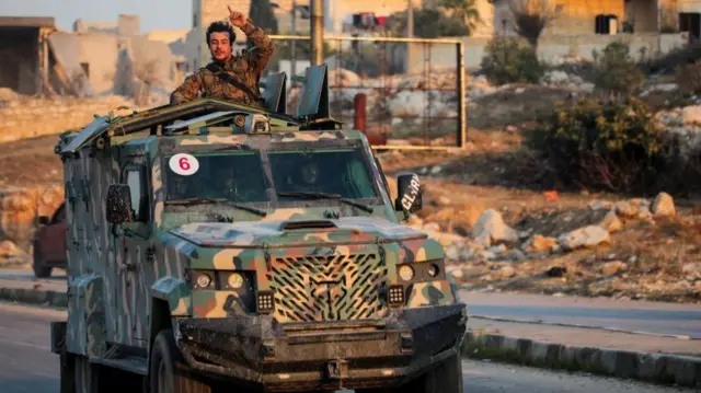 A rebel led by the Islamist militant group Hayat Tahrir al-Sham stands in the back of a vehicle in al-Rashideen, Aleppo province, Syria November 29, 2024. R