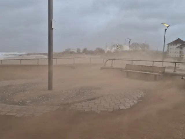 Sand blown onto the pavement and roads in Minehead. A bench and railings can be seen in the shot. The air is dusty and visibility is bad.