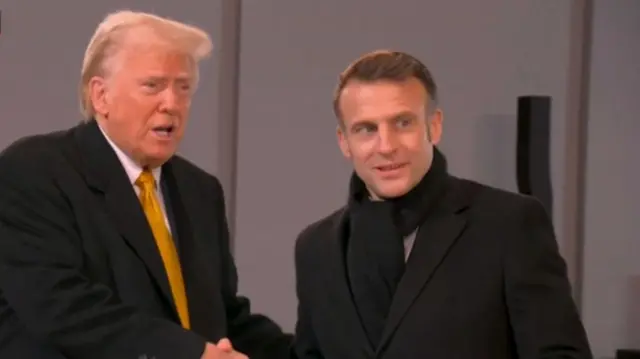 Trump shakes hands with Macron as he arrives at Notre Dame for the ceremony. They're both in black suits