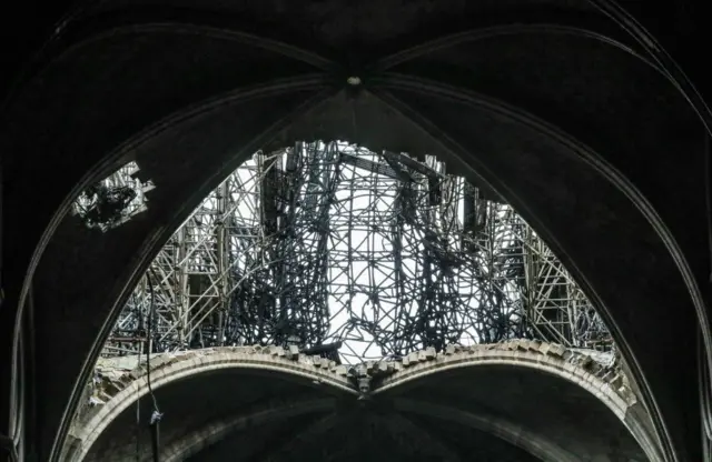 Section of the roof of Notre-Dame Cathedral is damaged, showing pipes and beams. The roof is so damaged that the sky is clearly visible through it